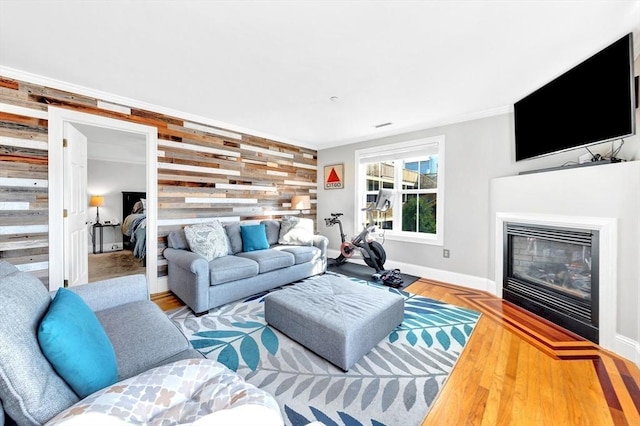 living area with wood finished floors, crown molding, wood walls, baseboards, and a glass covered fireplace