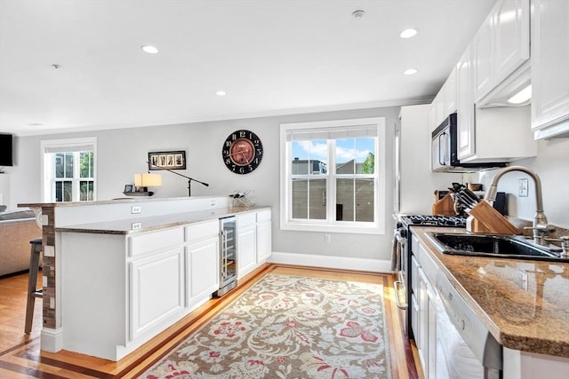 kitchen with wine cooler, dishwasher, a sink, white cabinets, and light wood-type flooring