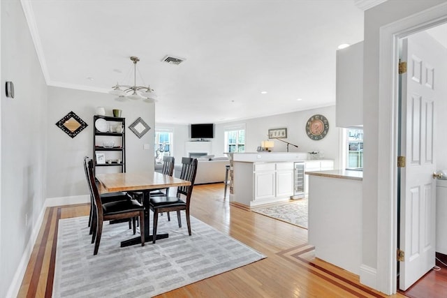 dining space featuring wine cooler, ornamental molding, light wood finished floors, and visible vents