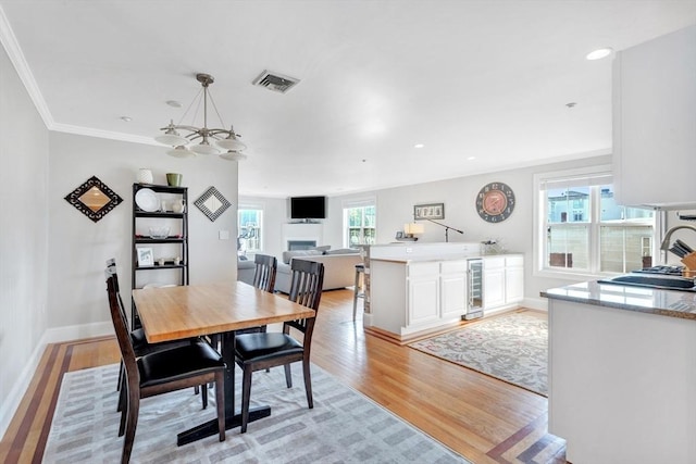 dining space with wine cooler, ornamental molding, visible vents, baseboards, and light wood-style floors