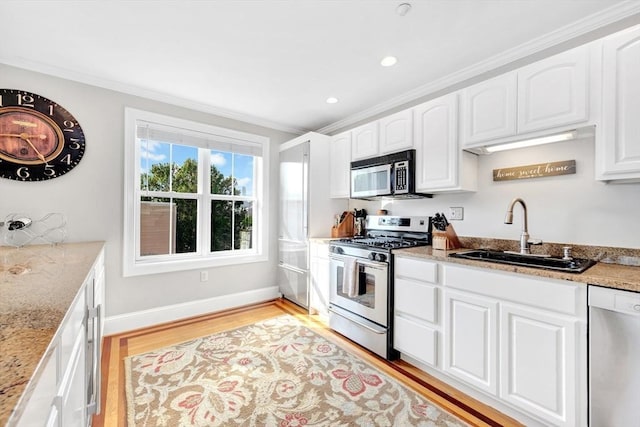 kitchen with light stone countertops, light wood-style flooring, ornamental molding, a sink, and stainless steel appliances