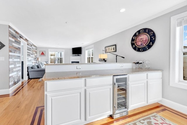 bar with light wood finished floors, beverage cooler, baseboards, and ornamental molding