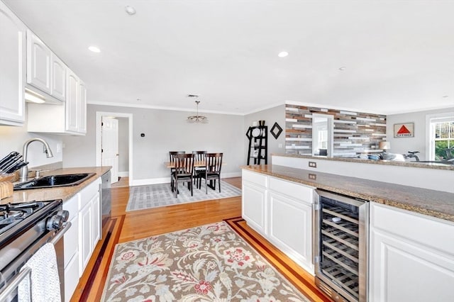 bar with wine cooler, light wood-style flooring, a sink, wet bar, and appliances with stainless steel finishes