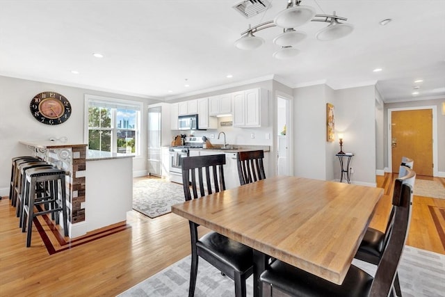 dining space featuring crown molding, light wood-type flooring, visible vents, and baseboards