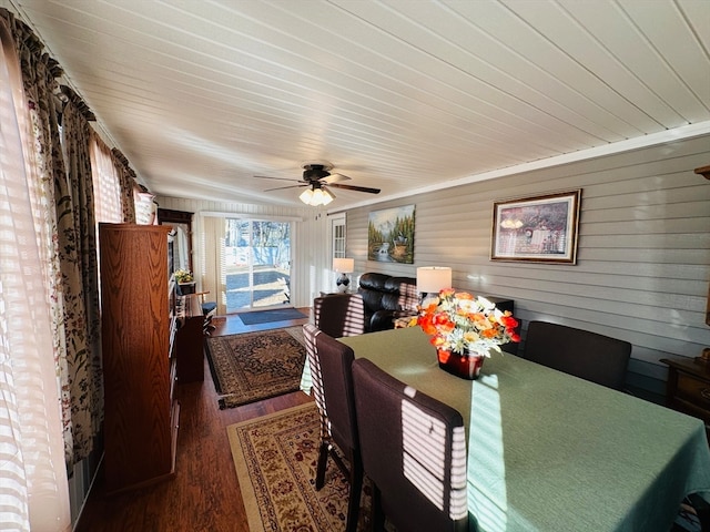 dining space with dark wood-type flooring, ceiling fan, and wood walls