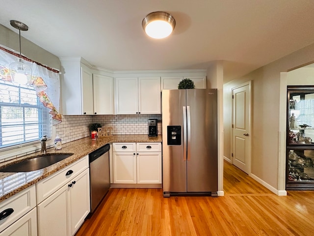 kitchen with appliances with stainless steel finishes, pendant lighting, sink, white cabinets, and light hardwood / wood-style flooring