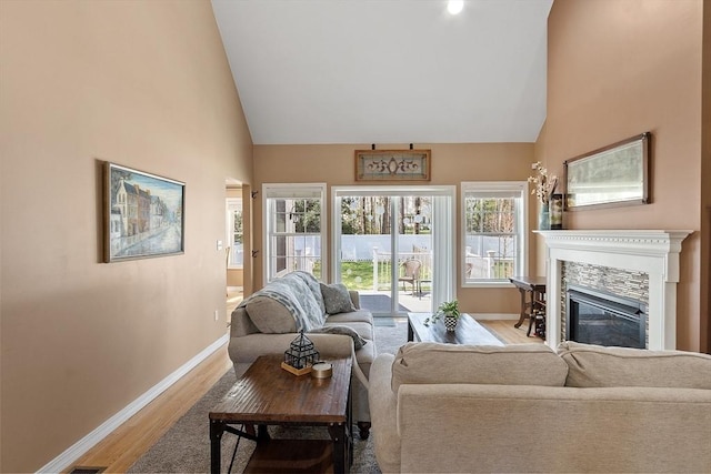 living room featuring a glass covered fireplace, high vaulted ceiling, wood finished floors, and baseboards