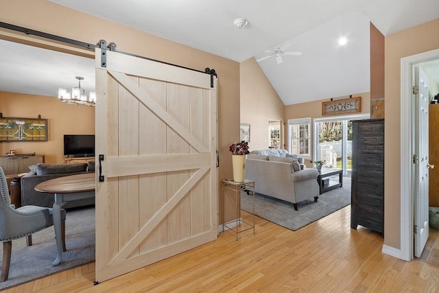 living room featuring light wood finished floors, a barn door, ceiling fan, high vaulted ceiling, and baseboards