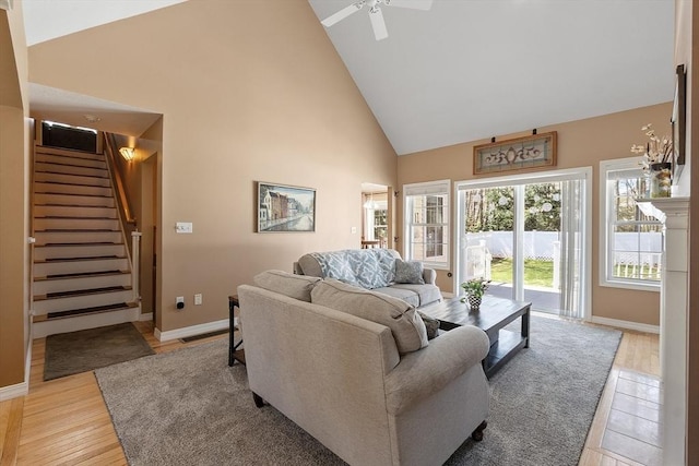living area with light wood-style flooring, stairway, ceiling fan, baseboards, and high vaulted ceiling