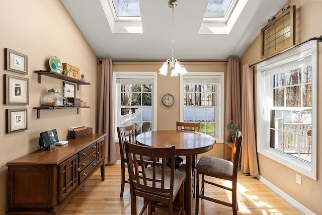 dining area featuring a notable chandelier, vaulted ceiling with skylight, and light wood-style floors