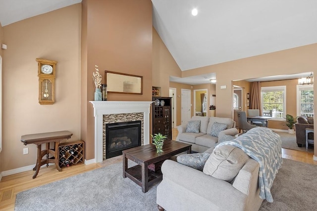 living room featuring baseboards, high vaulted ceiling, light wood-style flooring, and a glass covered fireplace