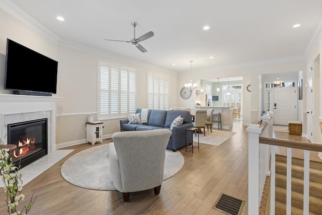 living room featuring ceiling fan with notable chandelier, ornamental molding, and light hardwood / wood-style floors