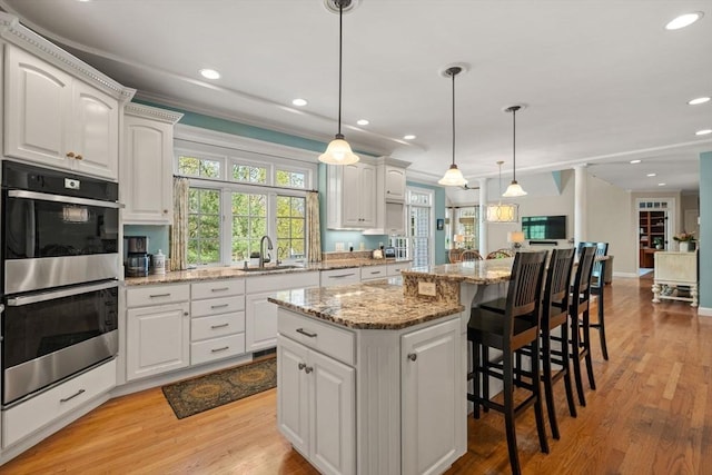 kitchen with double oven, a sink, white cabinets, recessed lighting, and crown molding