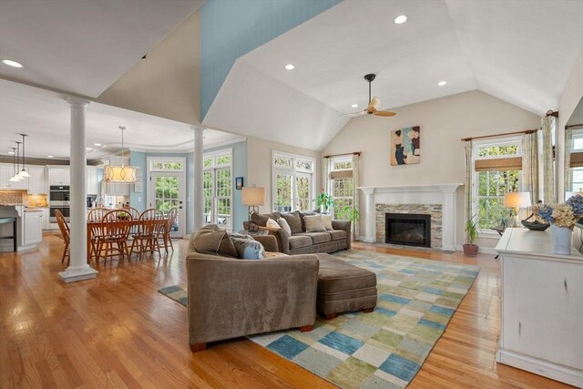living room with decorative columns, a ceiling fan, a fireplace, light wood finished floors, and vaulted ceiling