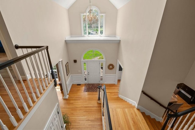 entryway with high vaulted ceiling, light wood finished floors, a chandelier, stairs, and wainscoting