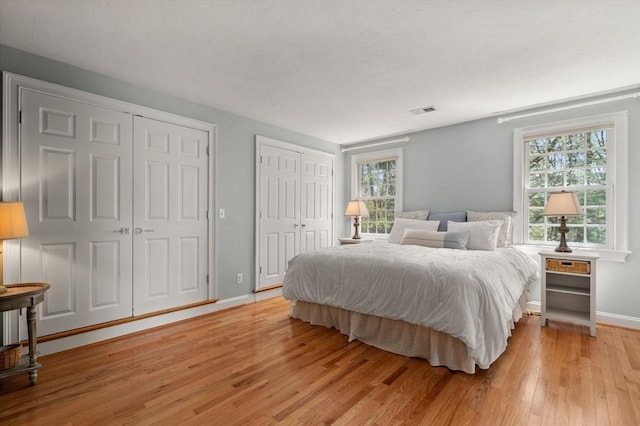 bedroom featuring light wood-type flooring, multiple closets, multiple windows, and baseboards