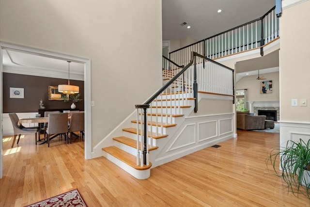 stairs with wood finished floors, a decorative wall, a fireplace, a towering ceiling, and a wainscoted wall