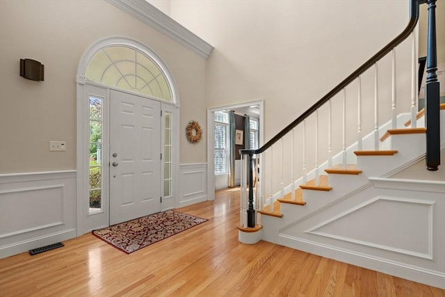 foyer featuring wood finished floors, a decorative wall, wainscoting, stairway, and a towering ceiling