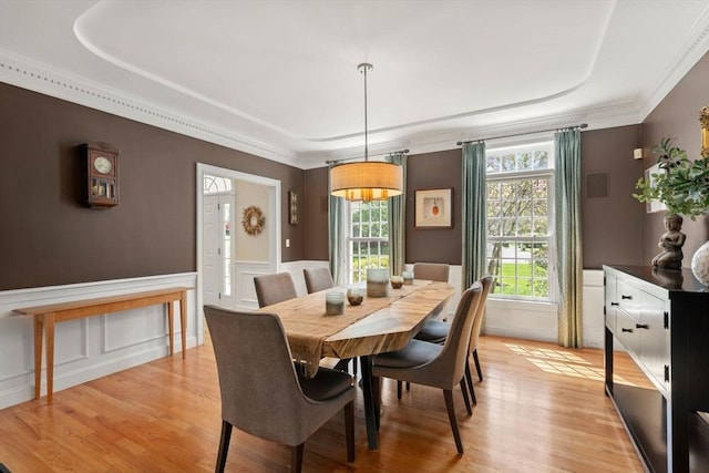 dining room featuring light wood finished floors, a wainscoted wall, a decorative wall, crown molding, and a raised ceiling