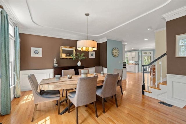 dining area featuring a decorative wall, crown molding, wainscoting, light wood finished floors, and stairway
