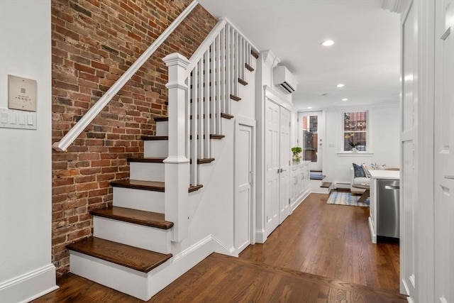 staircase featuring brick wall, baseboards, a wall unit AC, recessed lighting, and wood finished floors