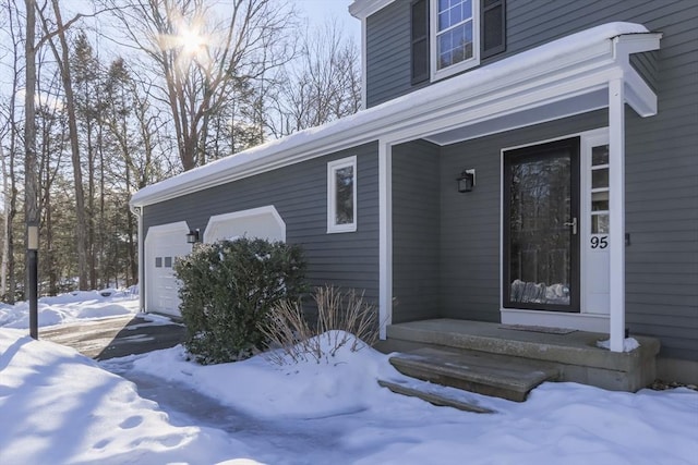 snow covered property entrance with an attached garage