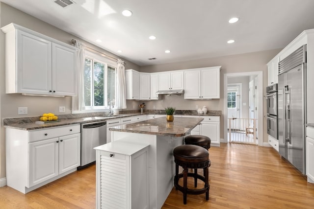 kitchen featuring stainless steel appliances, white cabinets, sink, light hardwood / wood-style flooring, and a center island