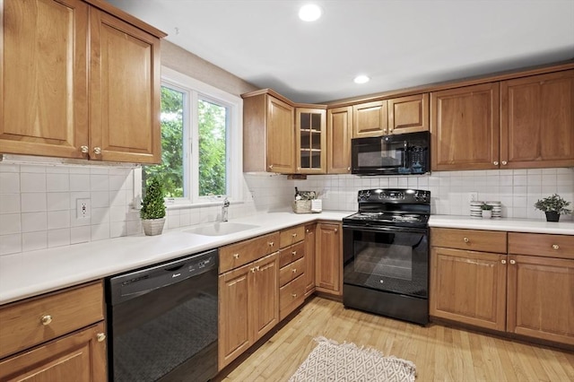 kitchen with black appliances, tasteful backsplash, a sink, and light wood finished floors