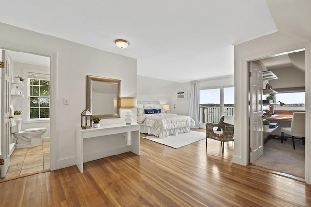 bedroom with multiple windows, hardwood / wood-style floors, ensuite bathroom, and access to exterior
