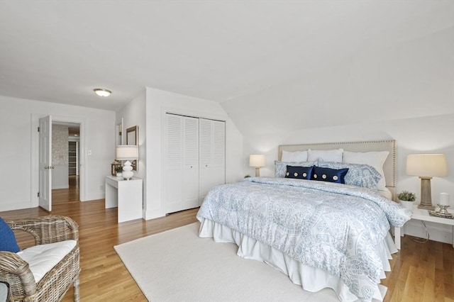 bedroom featuring lofted ceiling, baseboards, wood finished floors, and a closet