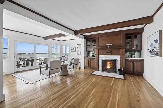 living area featuring a high end fireplace, baseboards, beamed ceiling, and light wood-style flooring