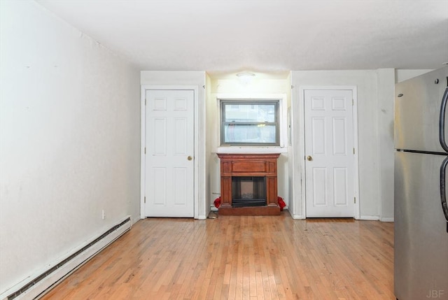 unfurnished living room featuring baseboard heating and light hardwood / wood-style floors