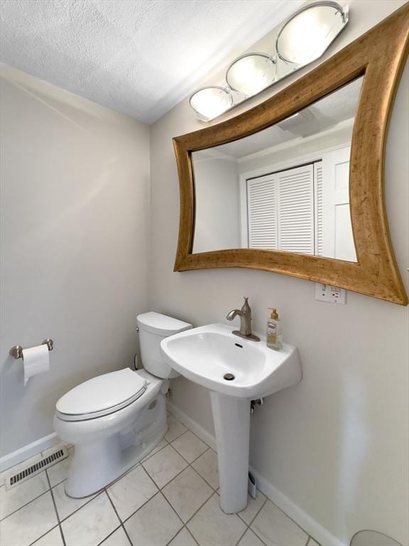 bathroom featuring visible vents, toilet, a textured ceiling, baseboards, and tile patterned floors