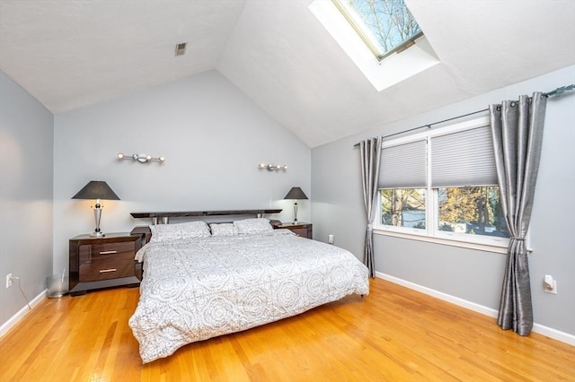 bedroom featuring light wood finished floors, baseboards, and lofted ceiling with skylight