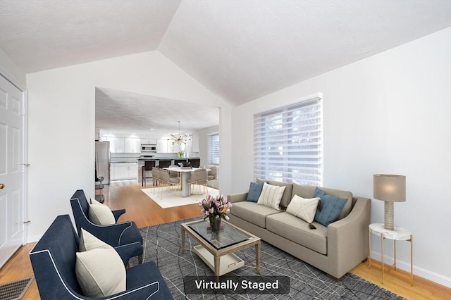 living area featuring visible vents, an inviting chandelier, vaulted ceiling, wood finished floors, and baseboards