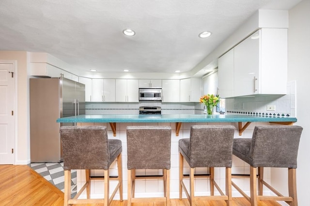 kitchen featuring appliances with stainless steel finishes, white cabinetry, a peninsula, and tasteful backsplash