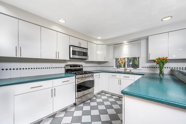 kitchen with appliances with stainless steel finishes, dark floors, white cabinetry, and a sink