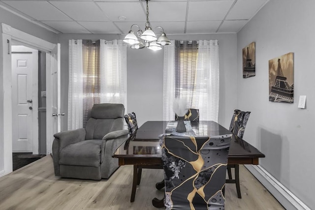 dining room featuring a drop ceiling, wood finished floors, a chandelier, and baseboards