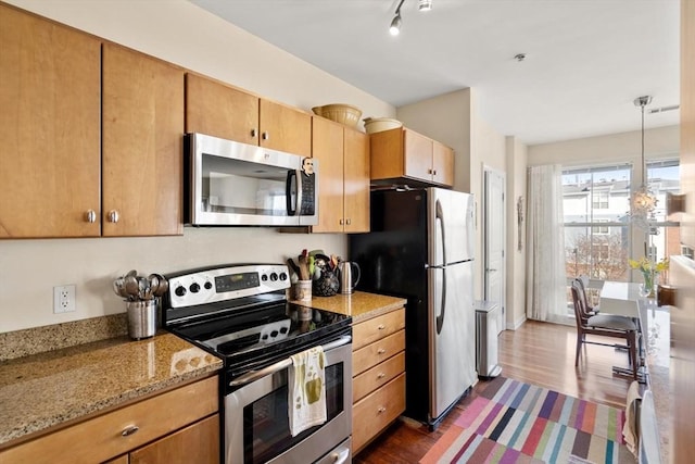 kitchen featuring dark wood-type flooring, light stone counters, rail lighting, hanging light fixtures, and stainless steel appliances