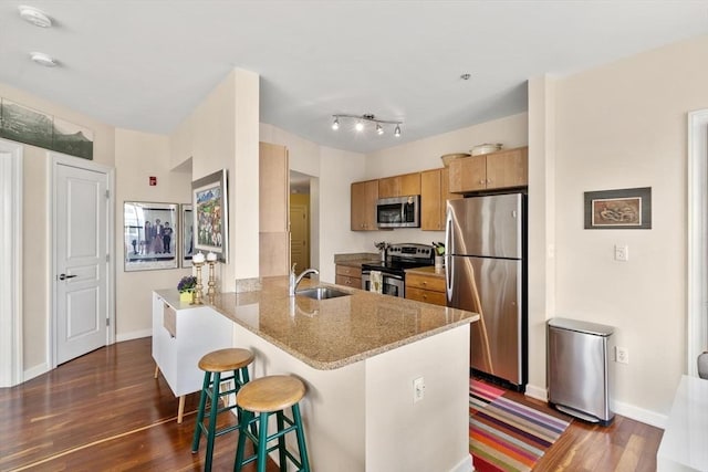 kitchen featuring a kitchen bar, a sink, dark wood finished floors, a peninsula, and appliances with stainless steel finishes