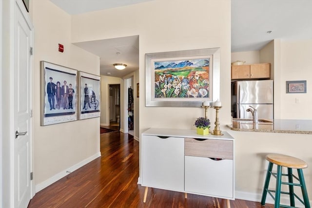 kitchen with dark wood-type flooring, baseboards, a breakfast bar area, freestanding refrigerator, and a sink