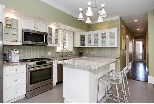 kitchen with a kitchen bar, stainless steel appliances, white cabinets, and a chandelier