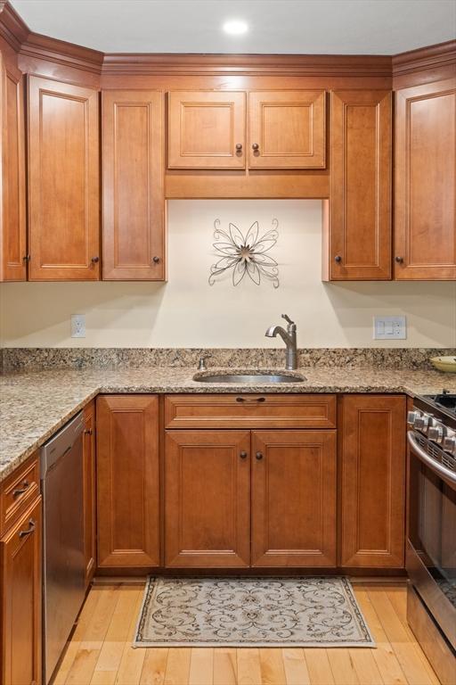 kitchen with a sink, appliances with stainless steel finishes, light wood-type flooring, light stone countertops, and brown cabinetry