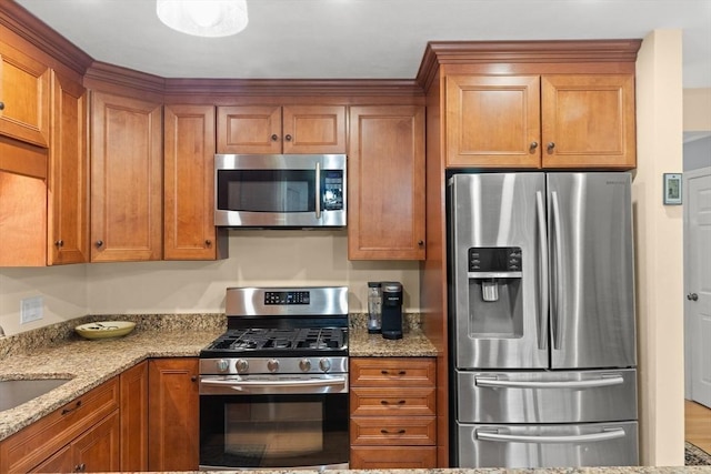 kitchen with stainless steel appliances, brown cabinets, light stone countertops, and a sink