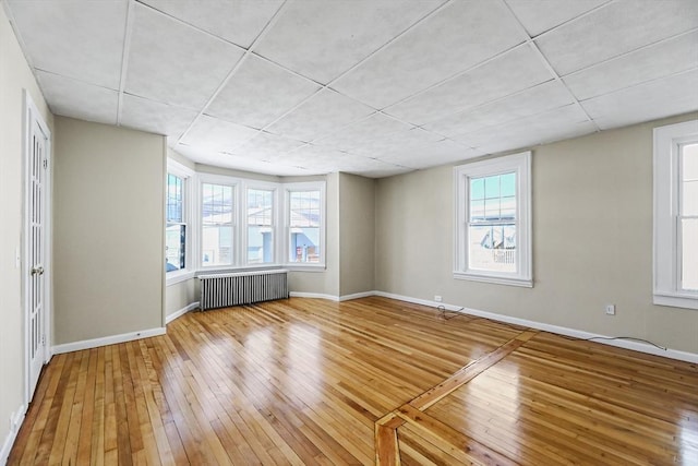 unfurnished room featuring a healthy amount of sunlight, radiator heating unit, baseboards, and wood finished floors