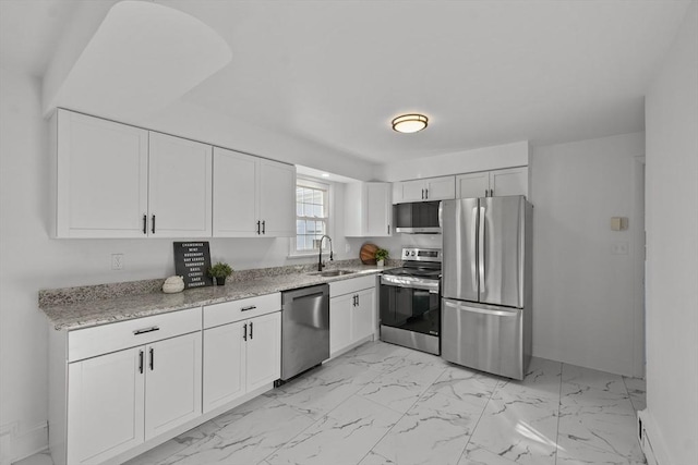 kitchen with white cabinetry, stainless steel appliances, light stone countertops, and sink