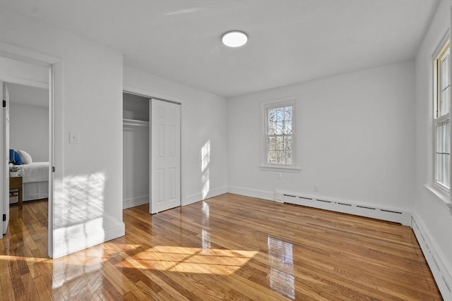 bedroom featuring a baseboard radiator, light hardwood / wood-style floors, and a closet