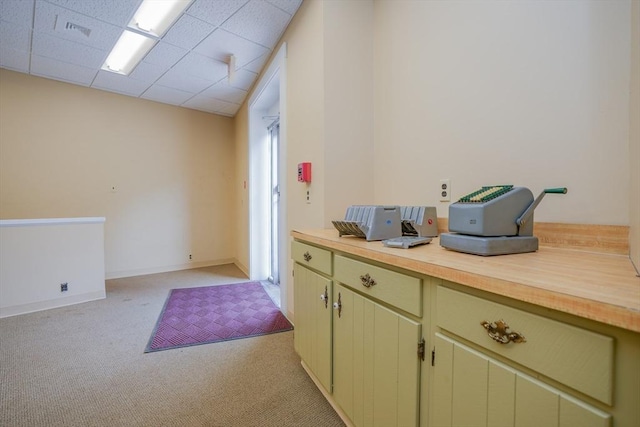 kitchen featuring butcher block countertops, light carpet, a drop ceiling, and green cabinetry