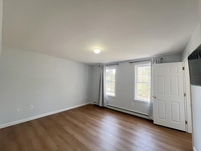 unfurnished room with a baseboard heating unit, baseboards, and wood finished floors