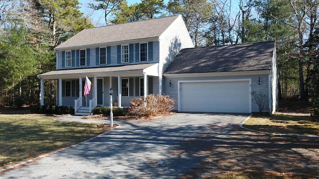 colonial home with a garage, covered porch, driveway, roof with shingles, and a front yard